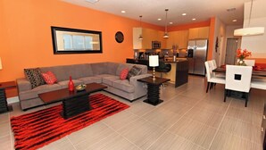 Una sala de estar moderna con un sofá gris, un tapete rojo y un comedor con sillas blancas y una mesa.
