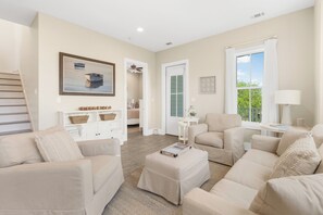 A spacious living room with a staircase, a large window with curtains, a painting, and a cozy seating area. - Sweet Escape, Sunny Days at Tupelo Honey / Gulf Views / Steps to Pool & Beach / 4 Bikes (Rosemary Bch)