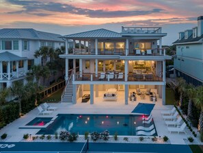 Une maison à plusieurs étages dotée d’une grande piscine, d’un espace salon extérieur et d’un patio couvert.