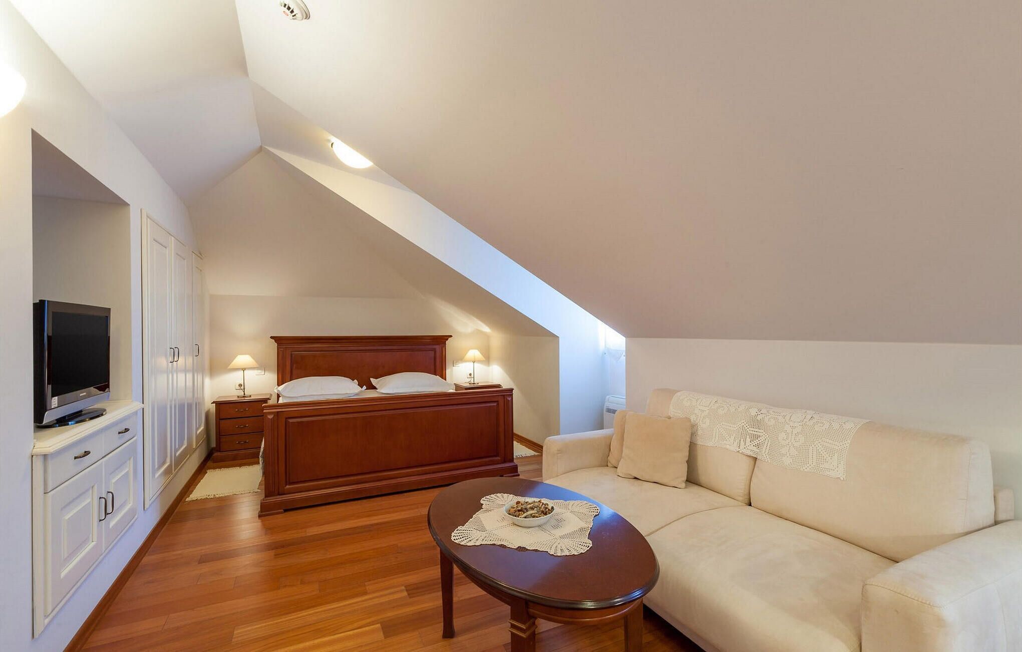 A bedroom with a bed, bedside lamps, a television, a sofa, and a coffee table.
