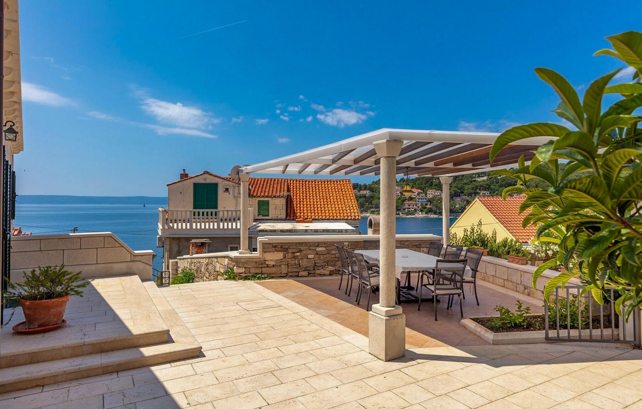 Zona de pati amb mobiliari exterior, una pérgola i vista al mar.