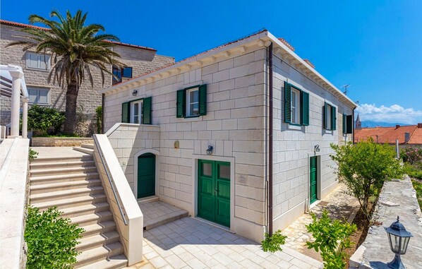 A two-story building with a stone facade, green shutters, and a staircase leading to the entrance.