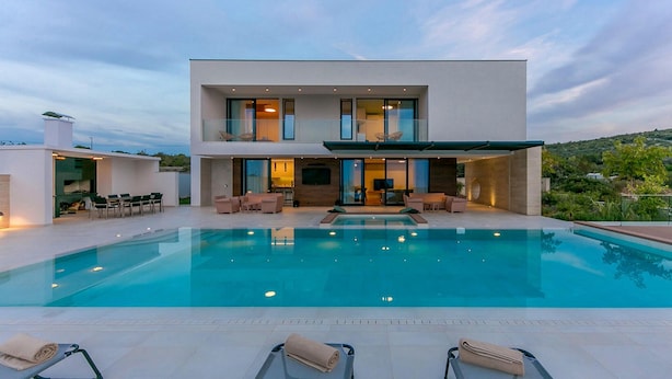 Una casa moderna de dos pisos con piscina, mobiliario exterior y vistas del paisaje circundante.