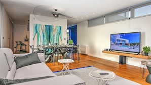 Una sala de estar moderna con un sofá, una mesa de comedor, sillas, un televisor y obras de arte en la pared.