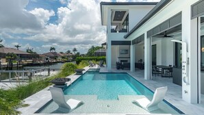 Ein modernes Haus mit Swimmingpool, Sitzgelegenheiten im Freien und Blick auf ein Gewässer.