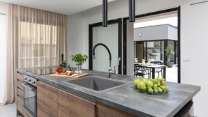 Una cocina moderna con una isla central, electrodomésticos de acero inoxidable y un amplio ventanal con cortinas.