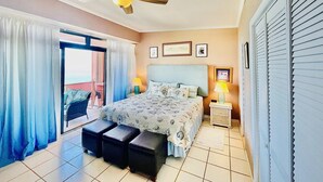 Una camera d'albergo con un letto, una ventola a soffitto, un comodino con una lampada e vista attraverso una porta in vetro.