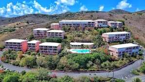 Un resort con diversi edifici, una piscina e uno sfondo collinare.