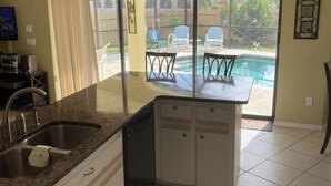 A kitchen with a built-in dishwasher, a double sink, and a view of a backyard with a pool and patio furniture. -  Florida Vacation Home or Private Room Rental with Fully Heated Pool (Port Charlotte)