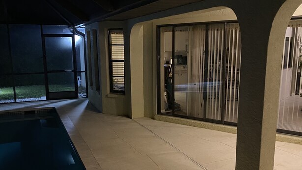 Área de piscina externa com piso de concreto, portas de vidro e guarda-corpo de metal.