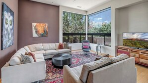 A modern living room with a sectional sofa, a coffee table, and a large window offering a view of trees and mountains.