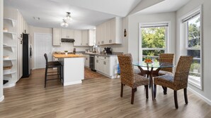 A modern kitchen with white cabinets, a central island, and a dining area with wicker chairs.