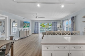 A spacious living area with a large TV, a dining table, and a ceiling fan.