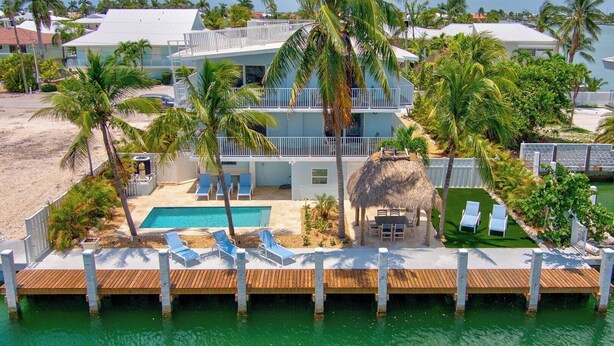 Ein Strandgrundstück mit Pool, Liegestühlen und einer Struktur mit Reetdach.