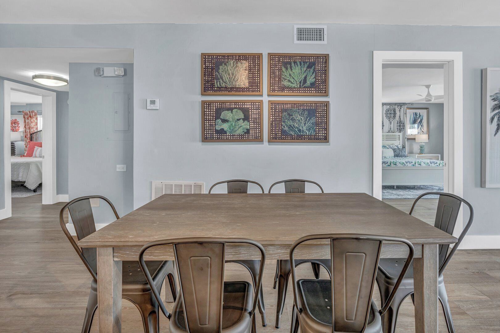A dining area with a wooden table and six chairs, a ceiling fan, and four framed botanical prints on the wall.