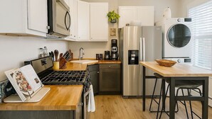 Een moderne keuken met witte kasten, roestvrijstalen apparatuur, een ingebouwde oven en een eethoek met een houten tafel en stoelen.