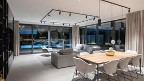 A modern living room with a wooden dining table, grey sofas, and a large window overlooking a pool. - Cozy home in Rovinjsko Selo with sauna (Rovinjsko Selo)