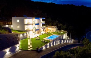 Ein modernes, mehrgeschossiges Haus mit Swimmingpool, einem gepflegten Rasen und einer Auffahrt zum Eingang.
