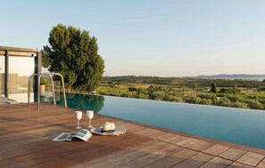 Une terrasse en bois avec une piscine à débordement donnant sur un paysage arboré et sur des bâtiments situés au loin.
