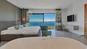 A modern bedroom with a large bed, a sitting area, a bathtub, and a TV.