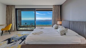 A hotel room with a large bed, a view of the sea, and a balcony with outdoor seating.