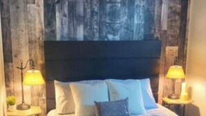Une chambre à coucher avec une tête de lit en bois, un lit recouvert d’une couvre-lit à motifs, deux lampes de chevet et une petite table sur laquelle est posée une plante.