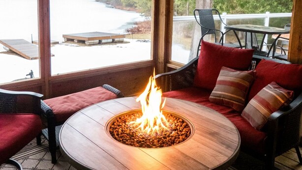Un espace de détente intérieur accueillant, avec un foyer, un plafond en bois et de grandes fenêtres donnant sur un lac.