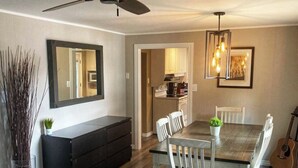 Un coin repas avec une table et des chaises en bois, un ventilateur de plafond, un meuble noir et une guitare.