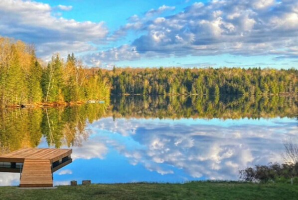 Eine Blockhütte am See mit einer Holzdielen-Terrasse und freiem Blick auf den umliegenden Wald.