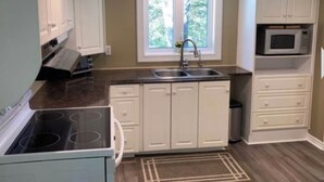 Une cuisine compacte avec des meubles blancs, un four à micro-ondes, une cuisinière et une fenêtre donnant sur un espace verdoyant.