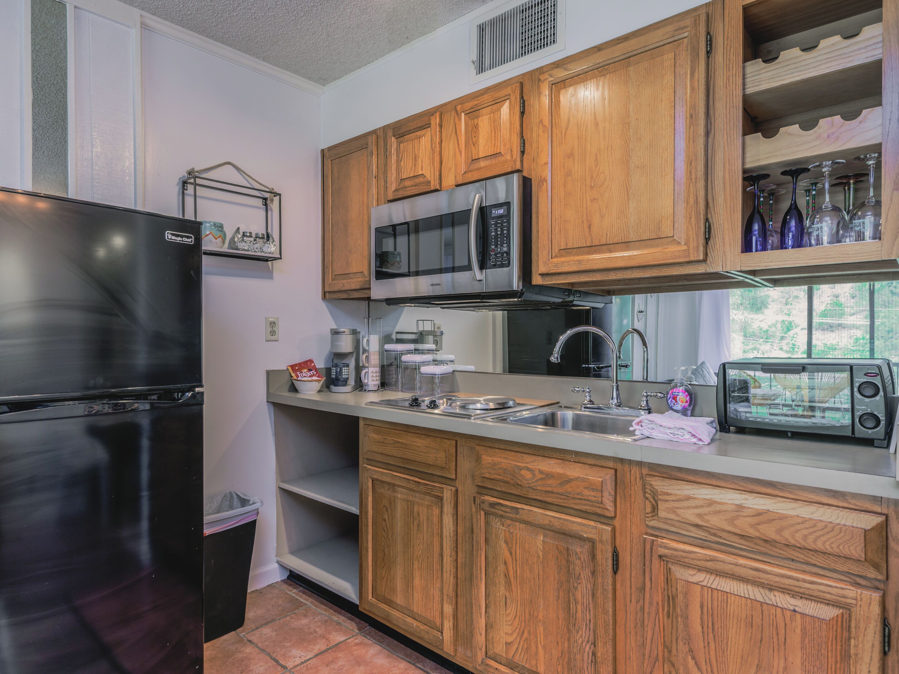 A compact kitchen with wooden cabinets, a refrigerator, a microwave, a toaster, and a sink.