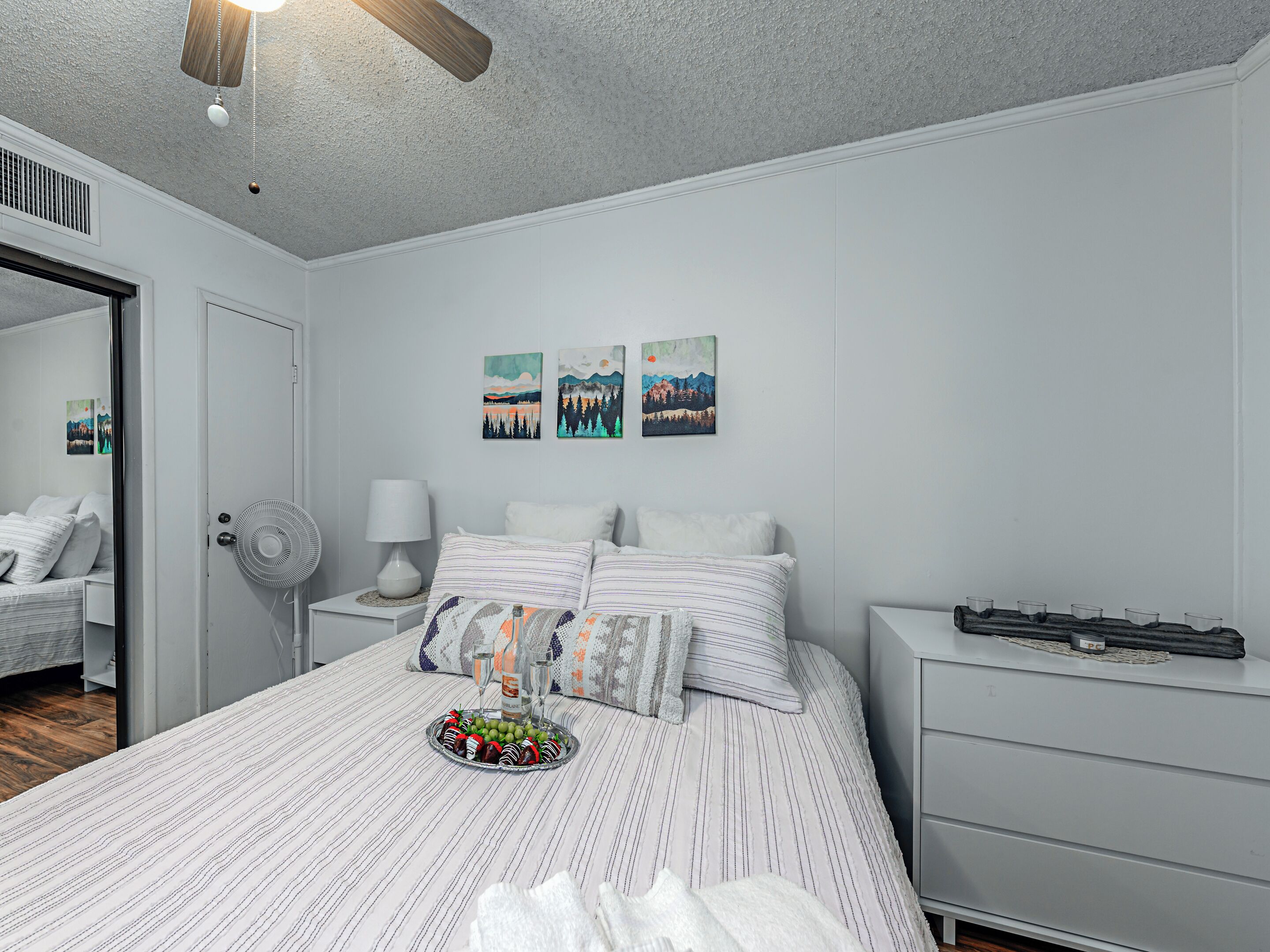 A bedroom with a bed, bedside table, lamp, and wall art.