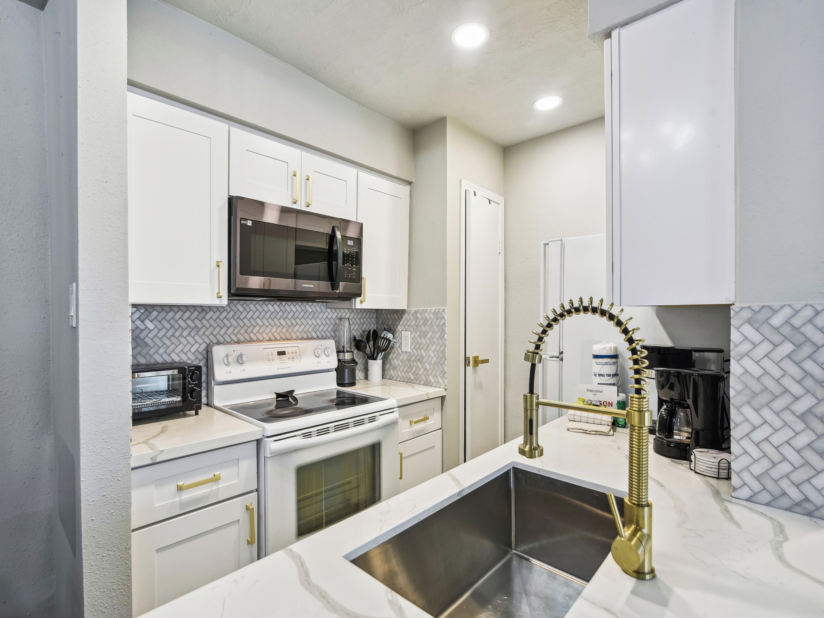 A modern kitchen with white cabinets, a stainless steel sink, a microwave, a stove, and a toaster.
