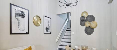A modern living room with a sofa, a dining table with chairs, a chandelier, and artwork on the walls.