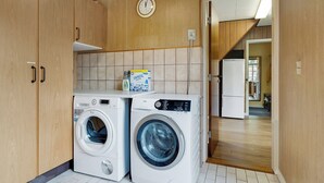 A laundry area with two washing machines, a clock, and wooden cabinets. - Cozy house close to Lalandia and Rødby Harbour (Rødby)