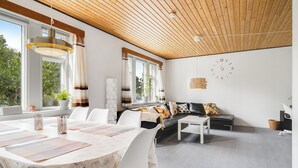 A modern living room with a dining area, wooden ceiling, large windows, and a clock on the wall. - Cozy house close to Lalandia and Rødby Harbour (Rødby)