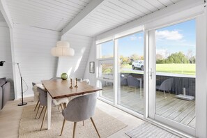 Ein Essbereich mit Holztisch, grauen Stühlen, einer weißen Pendelleuchte und Blick durch große Schiebetüren auf eine Terrassenanlage.