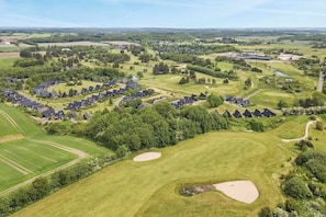 Vue aĂ©rienne dâun terrain de golf avec des maisons rĂ©sidentielles, des bunkers de sable et un grand bĂątiment.
