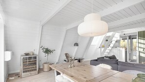 A high-ceilinged room with a wooden dining table, a sofa, and a hanging light fixture.