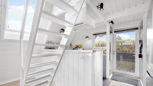 A modern interior with a white wooden staircase, a kitchen area, and a glass door leading to an outdoor deck.