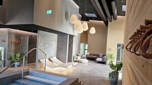 A modern indoor pool area with a lounge, seating, and a staircase leading to a spa area.