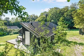 A small cabin with a sloped roof, surrounded by a grassy yard and dense trees.