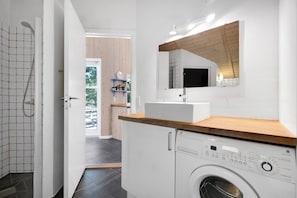 A modern bathroom with a shower, a sink, a washing machine, and a mirror. - Summer house in beautiful nature in Brunshuse (Haarby)