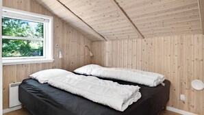 A bedroom with a wooden ceiling, a window, a bed with white bedding, and a bedside table.