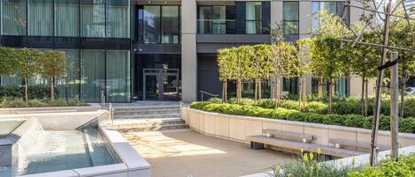 A modern building with a courtyard featuring a water feature, seating areas, and greenery.
