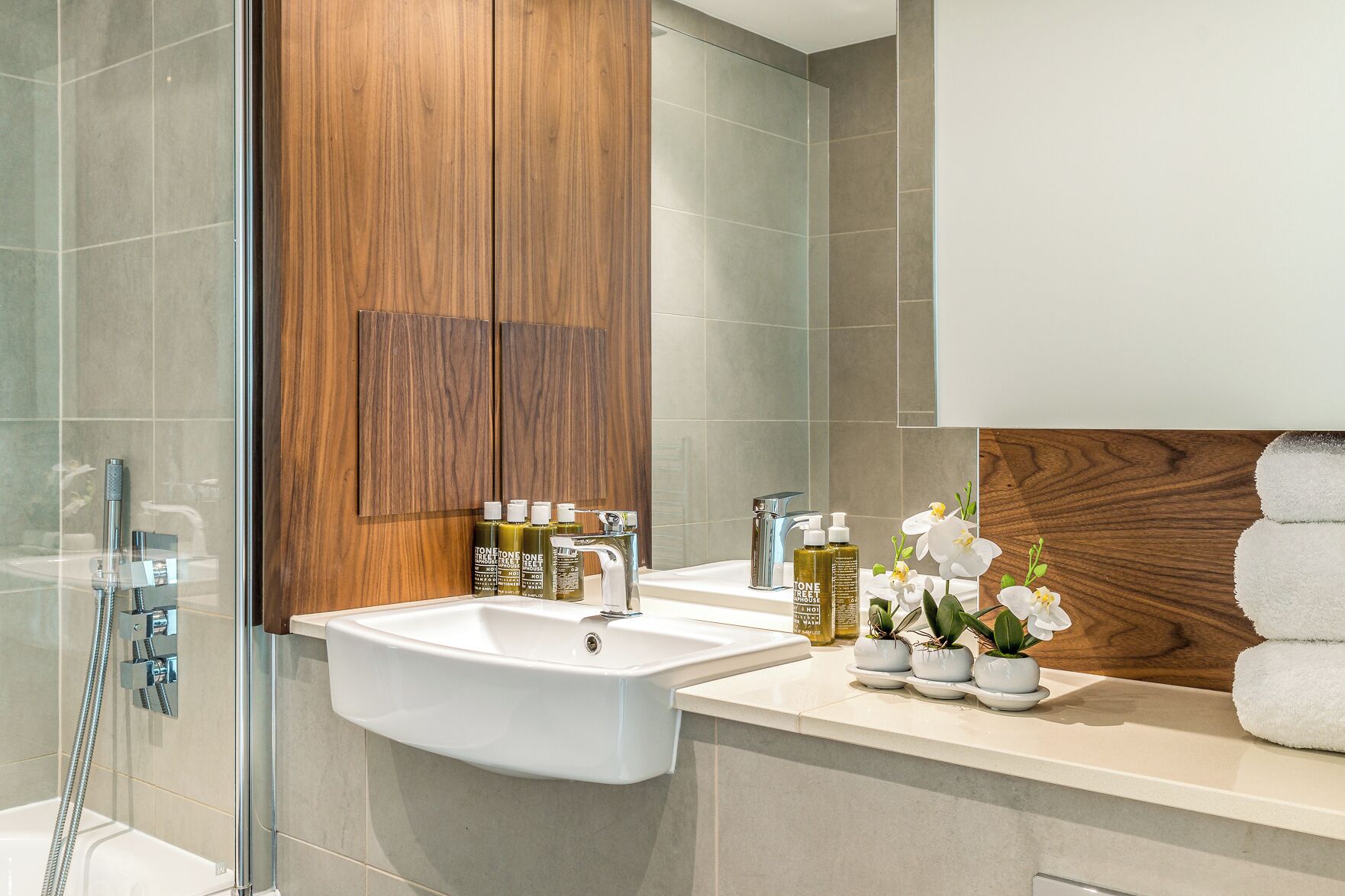 Een moderne badkamer met een douchecabine van glas, een witte wastafel en een houten badkamermeubel.