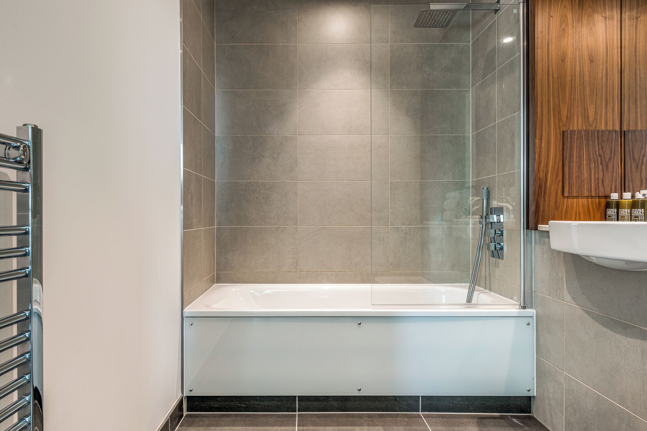 A modern bathroom with a glass-enclosed shower, a white bathtub, and a wooden vanity with a sink.
