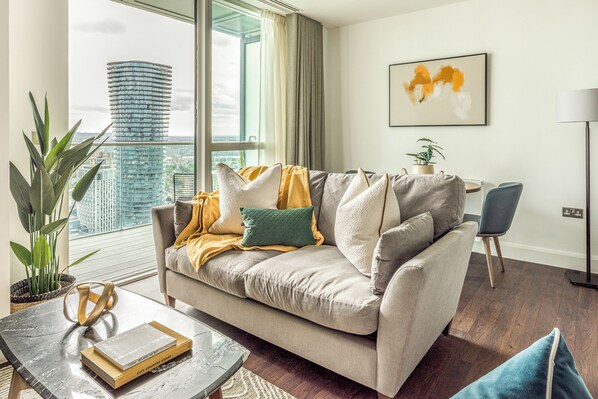 A modern living room with a sofa, a coffee table, and a view of a cityscape through large windows.
