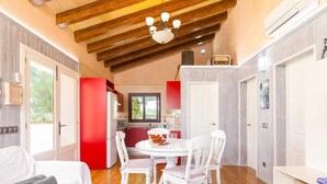 Une pièce chaleureuse avec un plafond en bois, une table à manger avec des chaises, un lit et un mur blanc agrémenté d’une étagère.