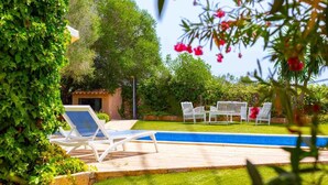 Un espace piscine avec des chaises longues et un petit bâtiment, le tout entouré de verdure.